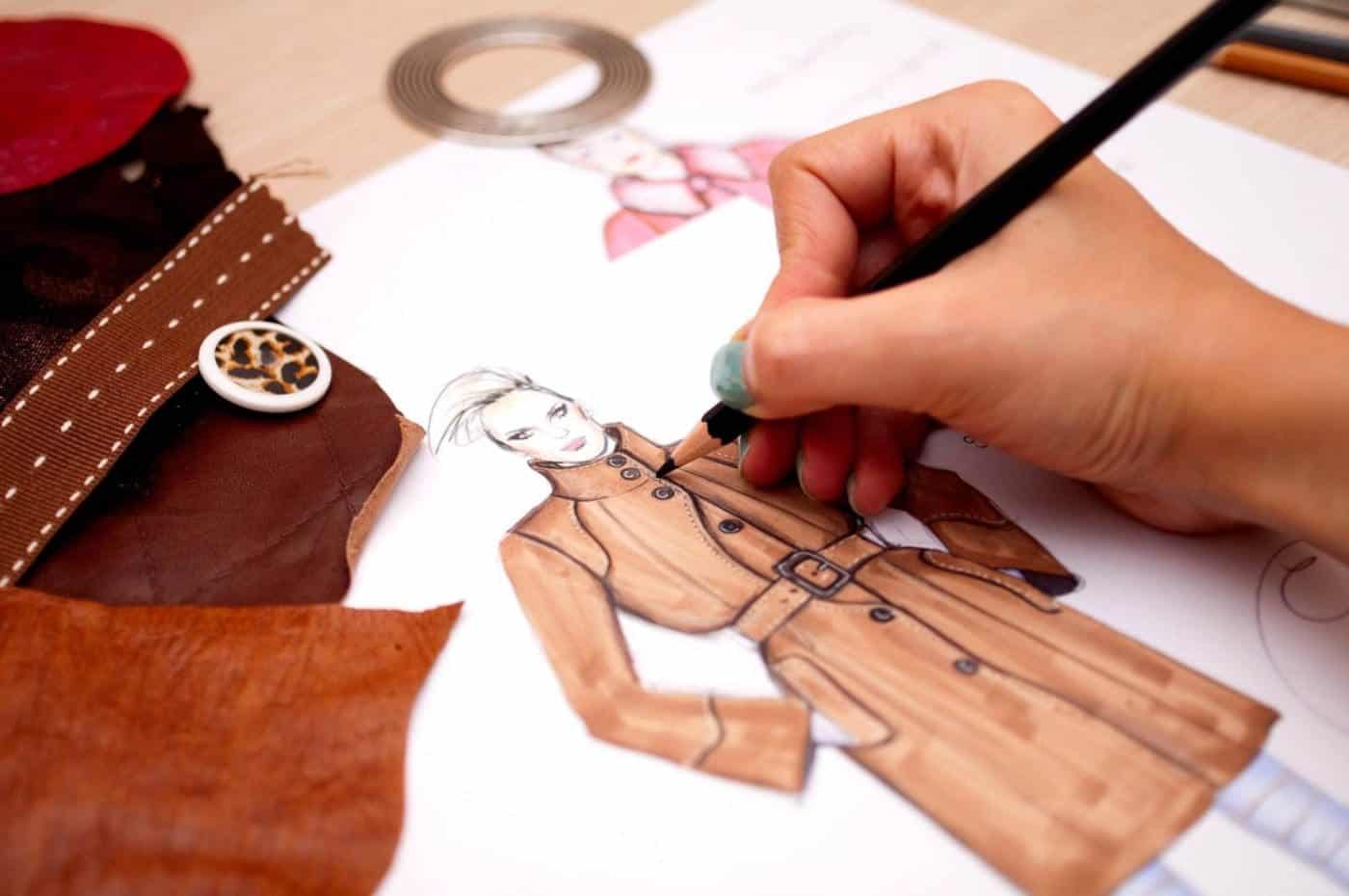 Designer sketching fashion illustration with pencil and swatches.