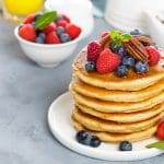 Fresh berry-topped pancakes with pecans on a plate.