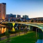 Adelaide skyline at dusk with illuminated buildings and river reflection.