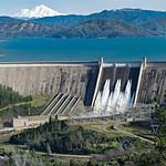 Shasta Dam with spillways open, scenic mountain lake view.