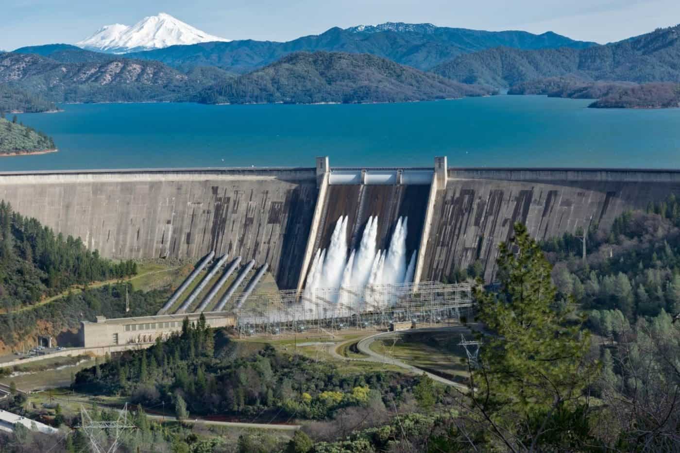 Shasta Dam with spillways open, scenic mountain lake view.