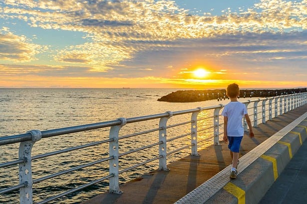 Boy walking on St. Kilda Jetty at sunset.
