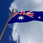 Australian flag waving against blue sky with clouds.
