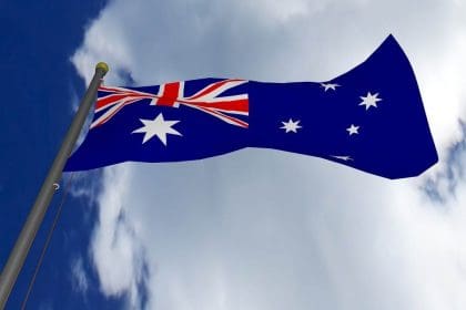 Australian flag waving against blue sky with clouds.