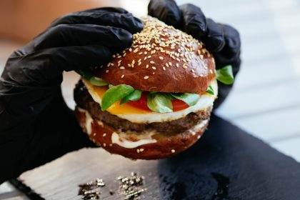 Hand in black gloves holding a gourmet burger.