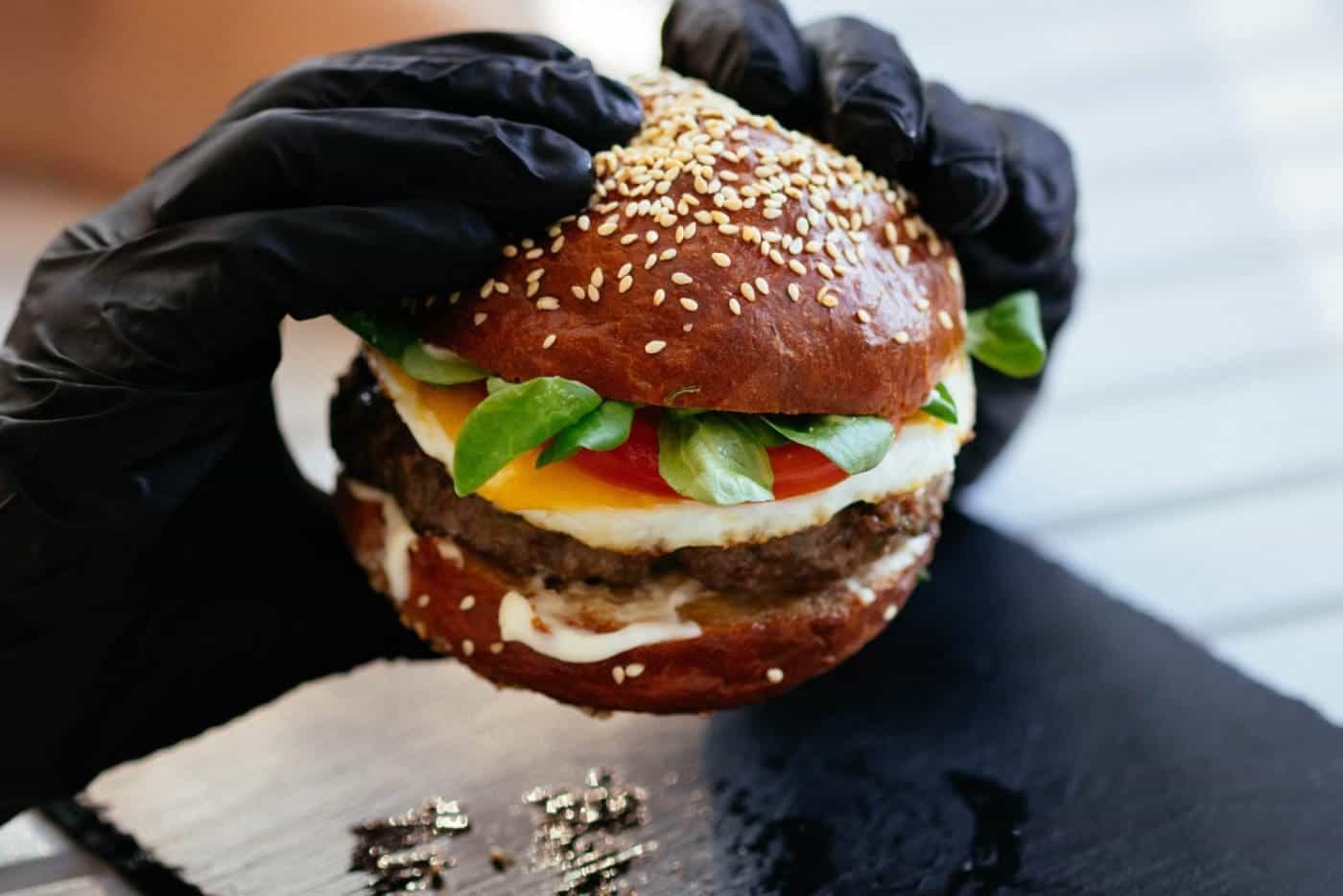 Hand in black gloves holding a gourmet burger.