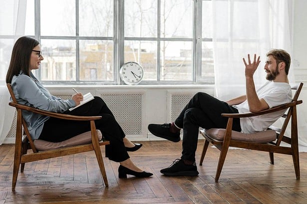 Two people having a conversation on wooden chairs.