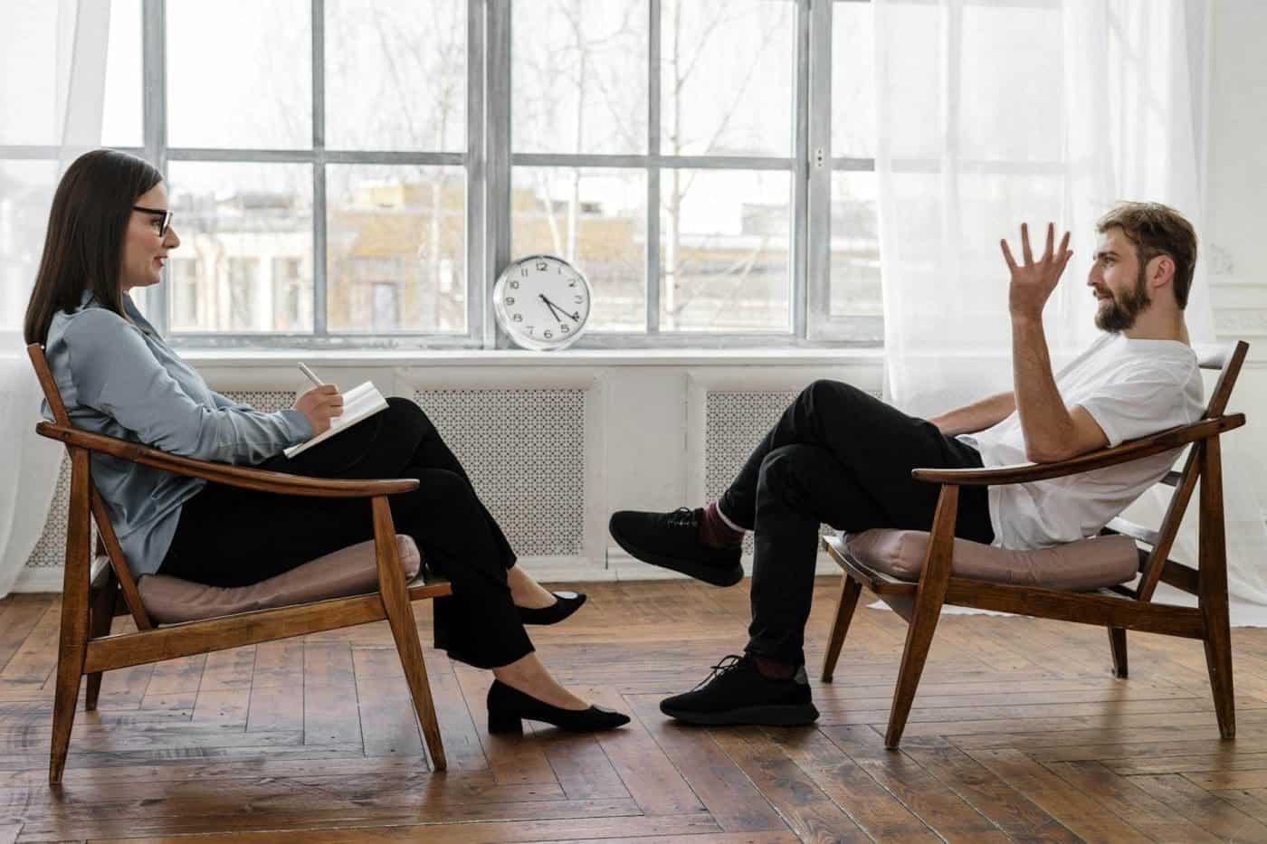 Two people having a conversation on wooden chairs.