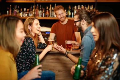 Diverse friends laughing and drinking at a cozy bar.