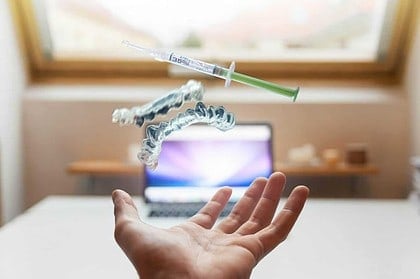 Hand with clear dental aligner and syringe hovering above.