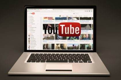 Laptop displaying YouTube homepage on screen against a dark background.