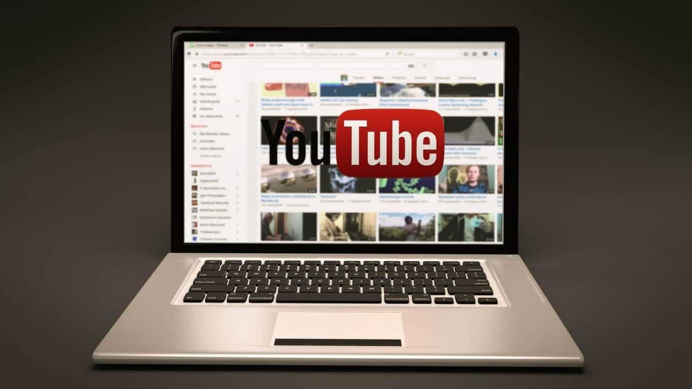 Laptop displaying YouTube homepage on screen against a dark background.