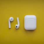 how to change the name on airpods: Apple AirPods with case on vibrant yellow background.