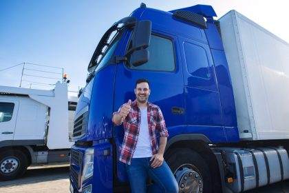 Happy truck driver giving thumbs up beside blue semi-truck.