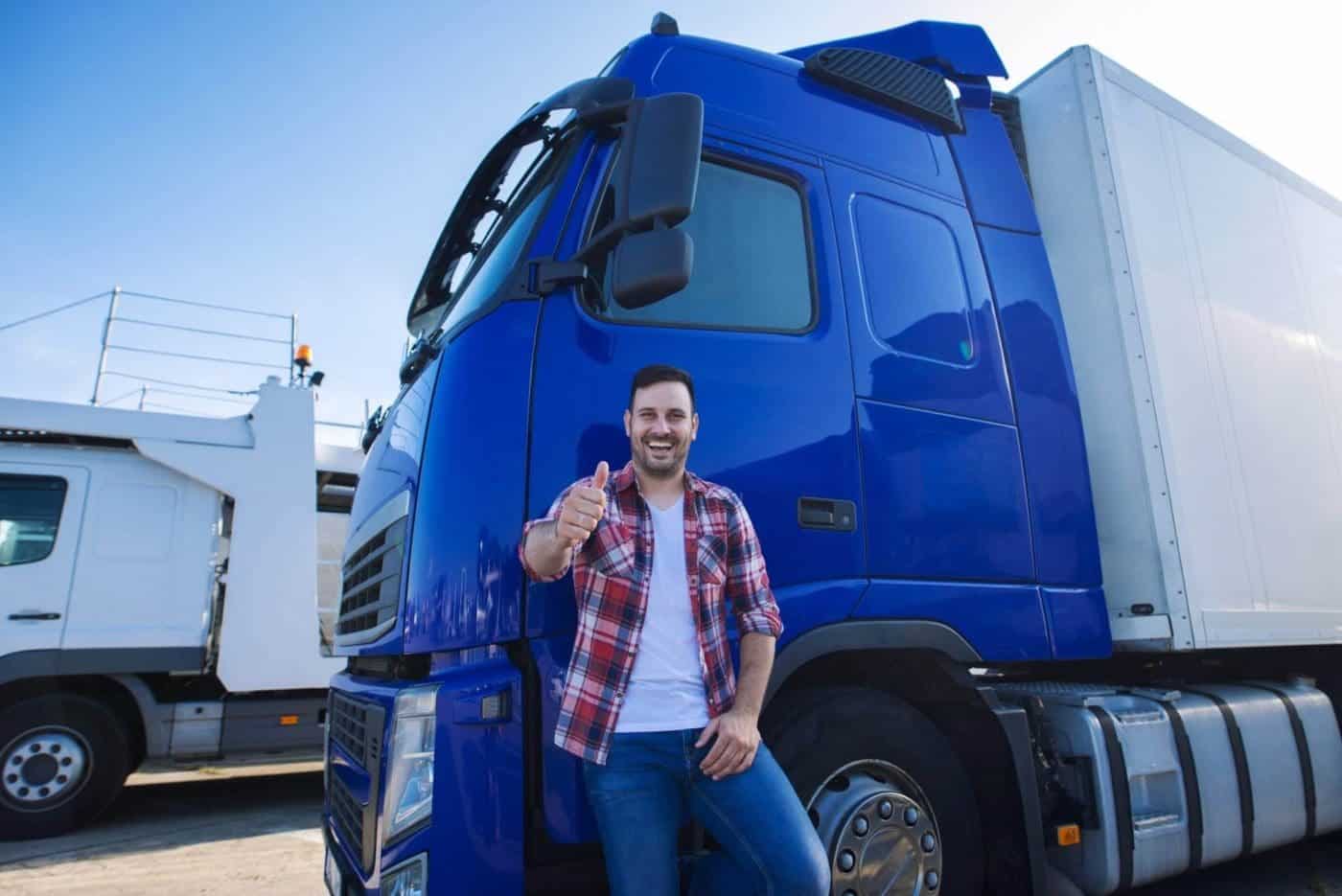 Happy truck driver giving thumbs up beside blue semi-truck.