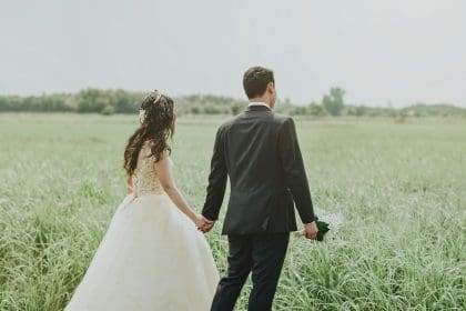 Bride and groom walking in field, outdoor wedding scene.
