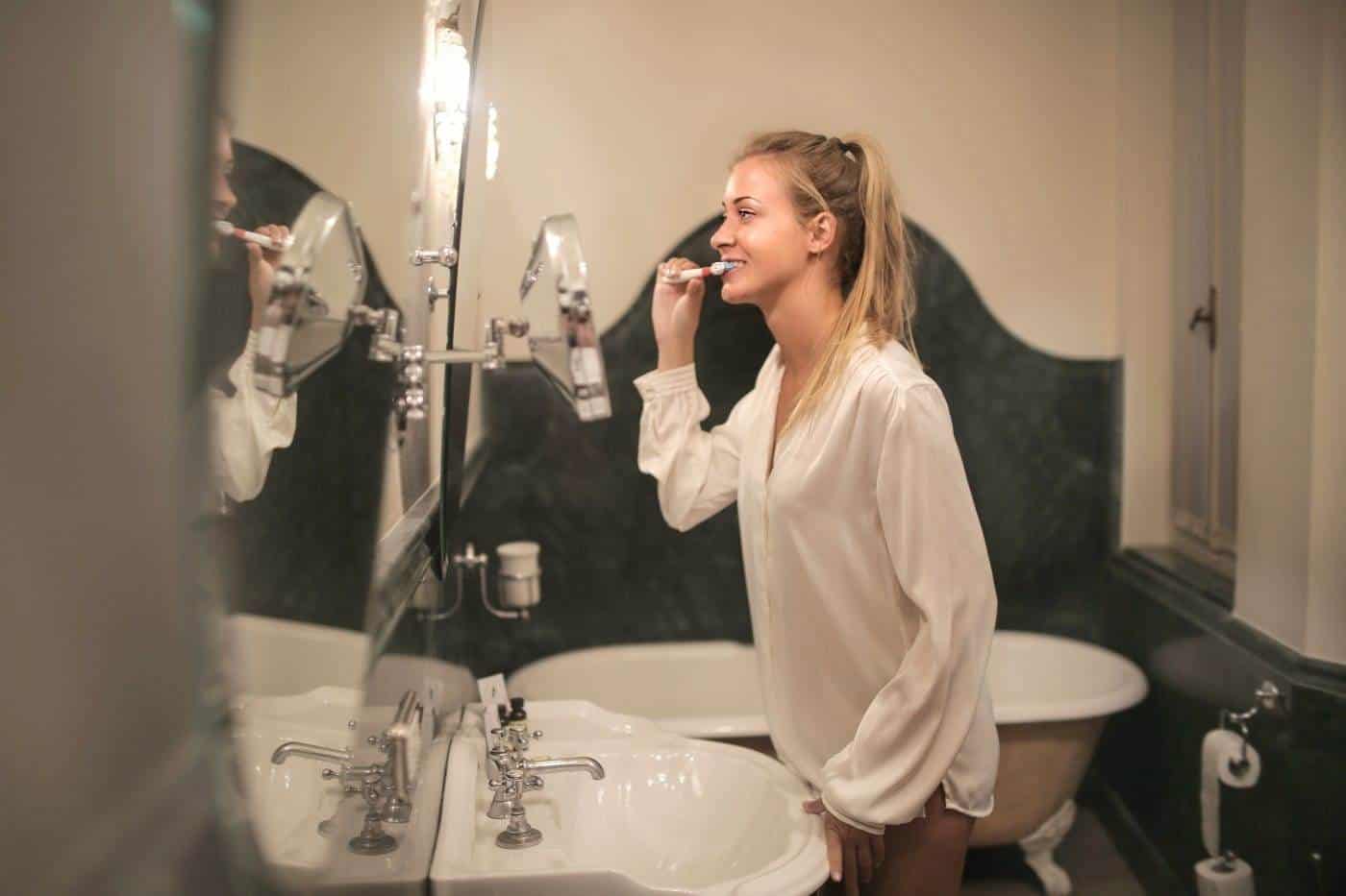 Woman brushing teeth in bathroom mirror